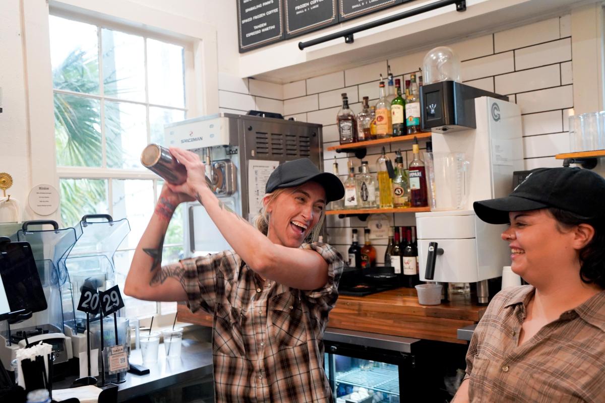Two women behind the counter of Tandem Coffee and Cocktails, one shakes a cocktail mixer as the other looks on, with bottles and coffeemakers behind.