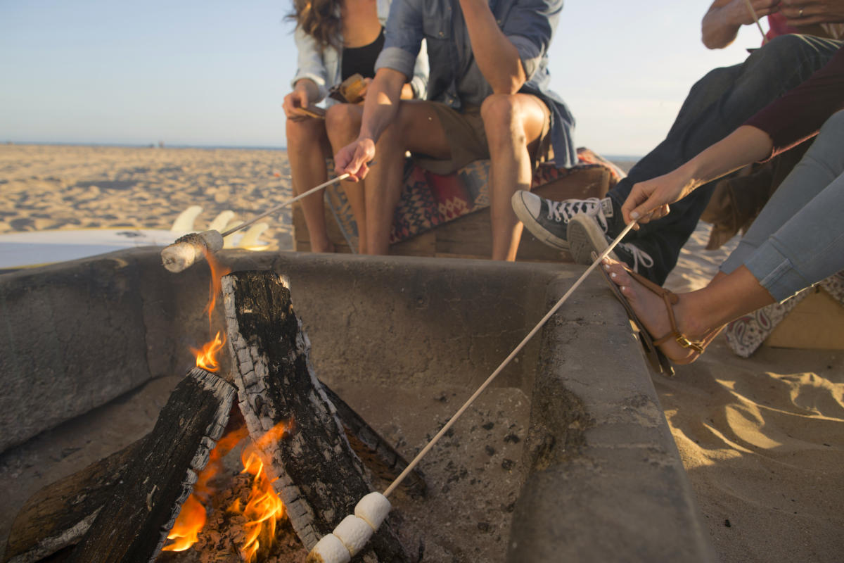 Friends roasting marshmallows on a beach bonfire in Huntington Beach