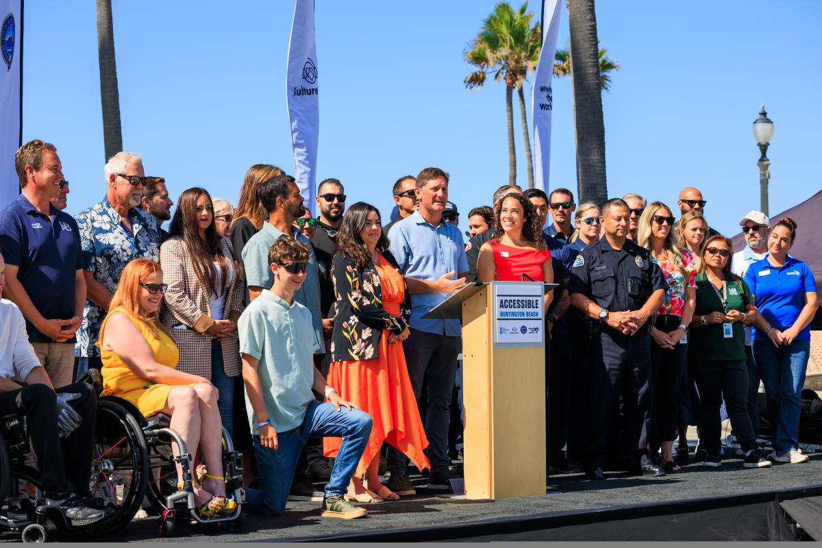 Group of people gathered around a podium on a sunny day outdoors.