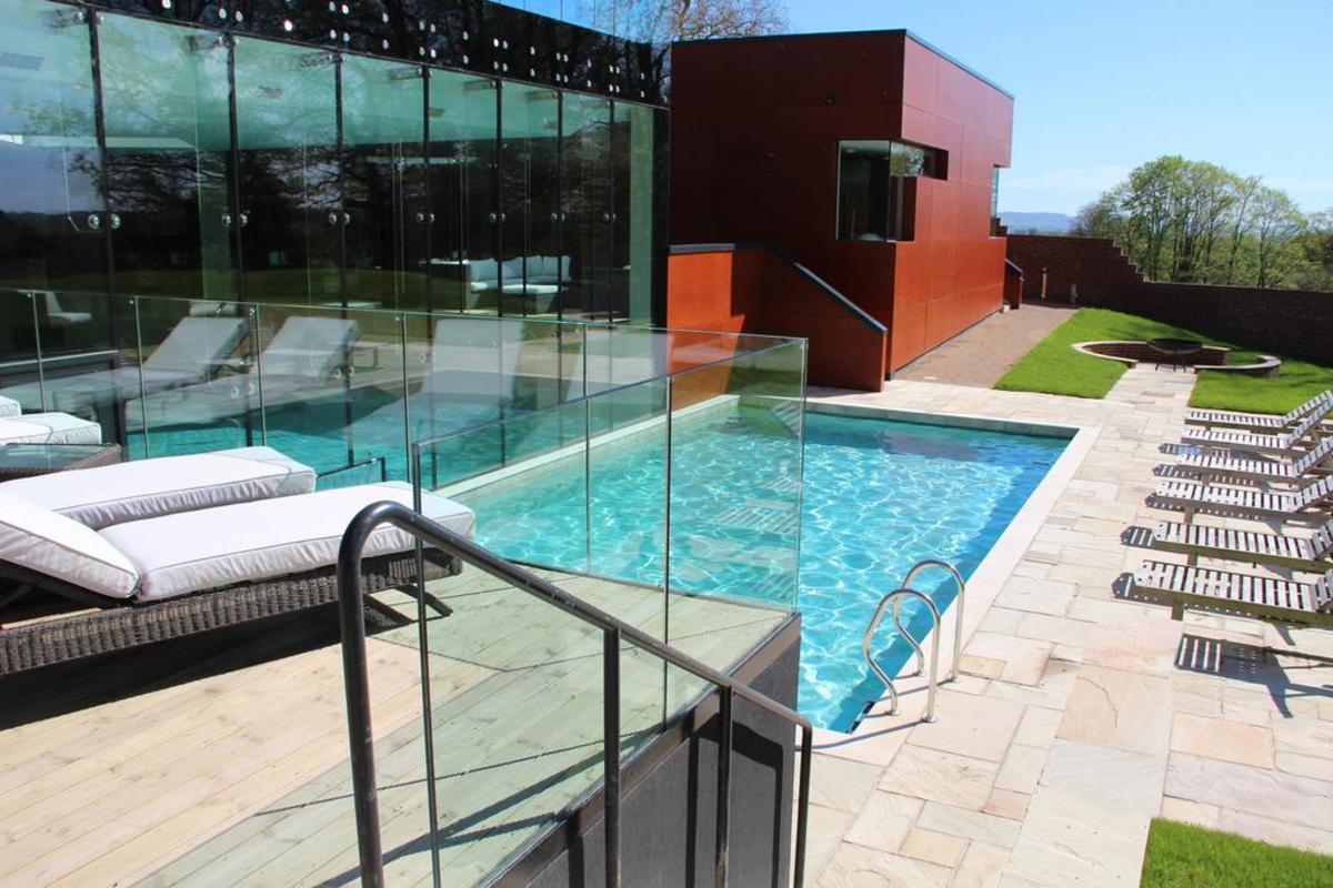 A sun lounger area surrounding an outdoor pool and glazed spa building at Ockenden Manor, Sussex