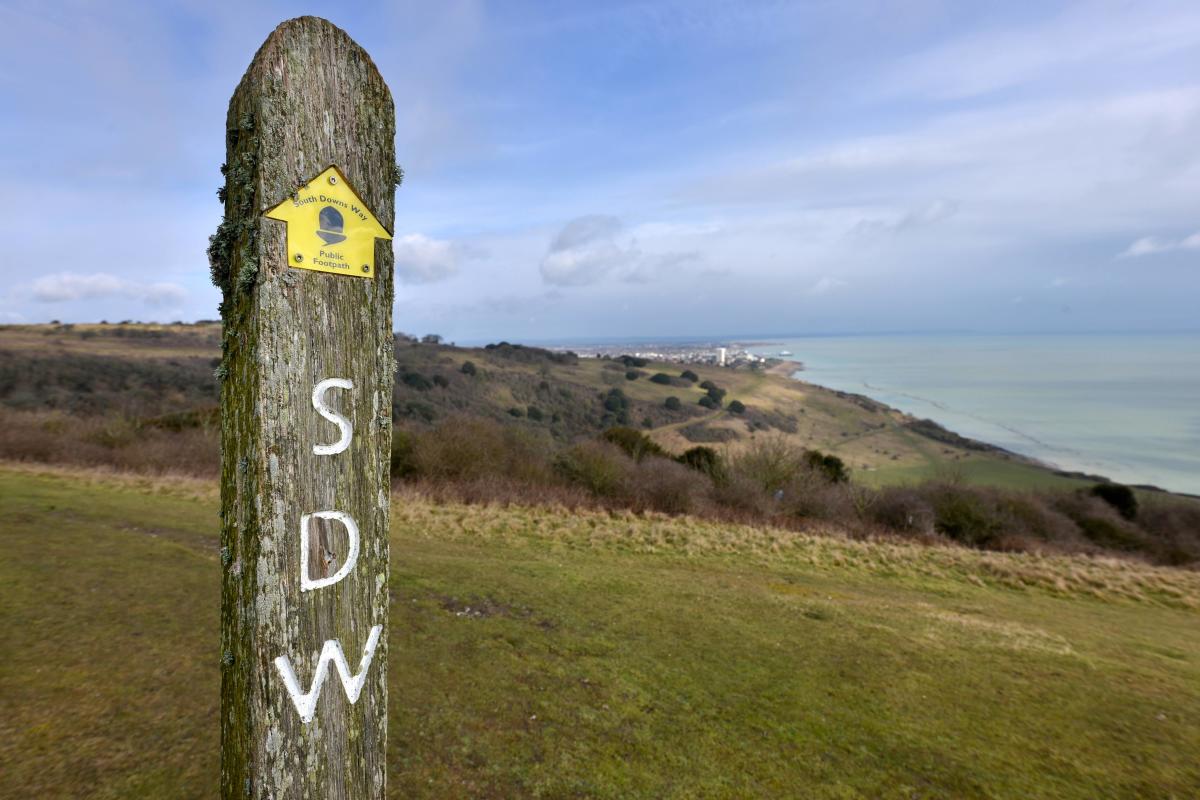 A wooden signpost with a yellow arrow for the South Downs Way, in Eastbourne
