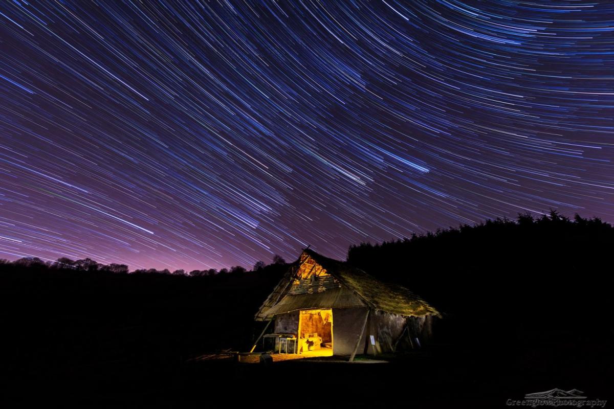 House illuminated from within with starwheels in the background against a silhoutted hill at nighttime in West Sussex