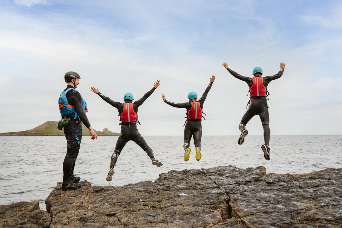 Group of people coasteering and jumping into water while instructor watches on