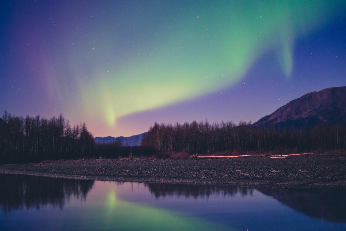The Northern Lights glow green and yellow against a blue and pink sky in Alaska
