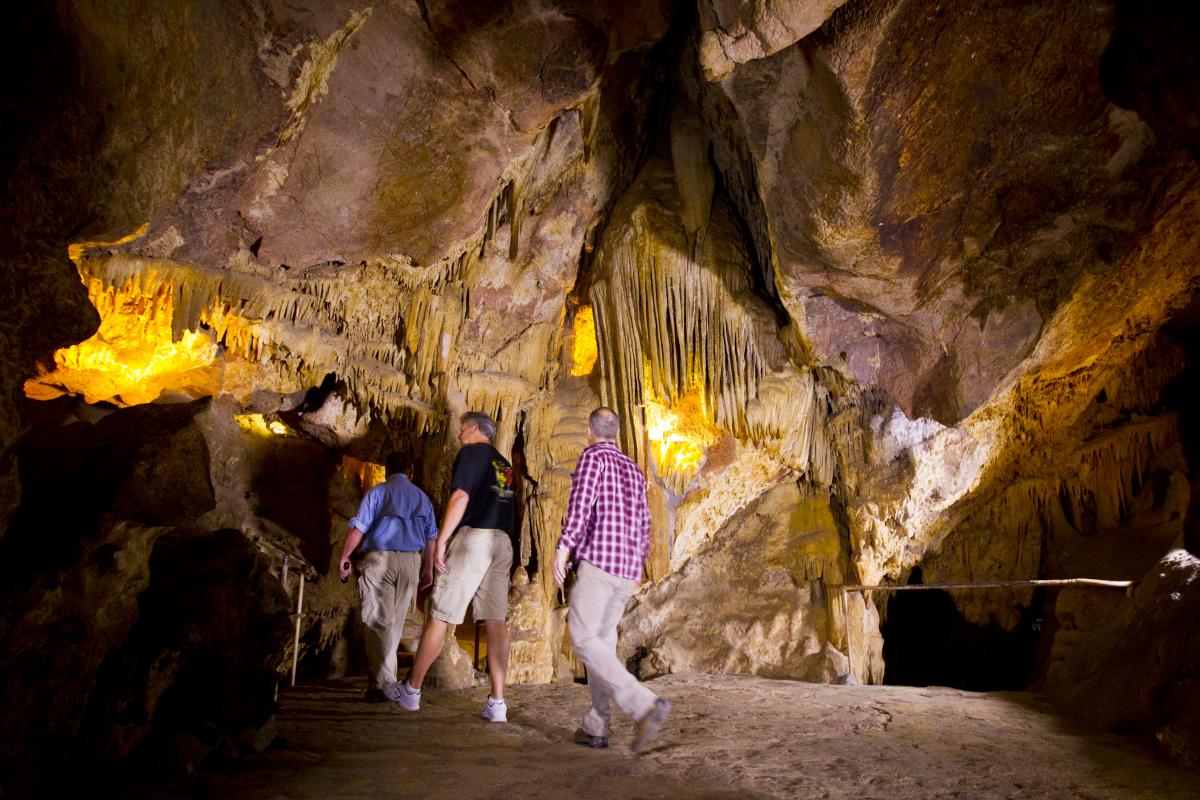 Three men waking in an open cave with stalagmites at Colossal Cave
