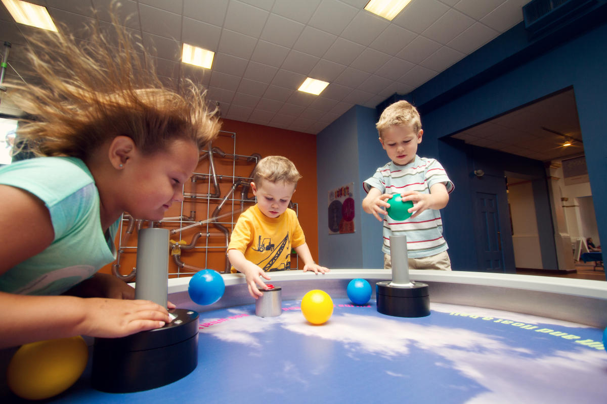 Three children playing with plastic balls on a table with tubes that blow air at the Childrens Museum in Tucson