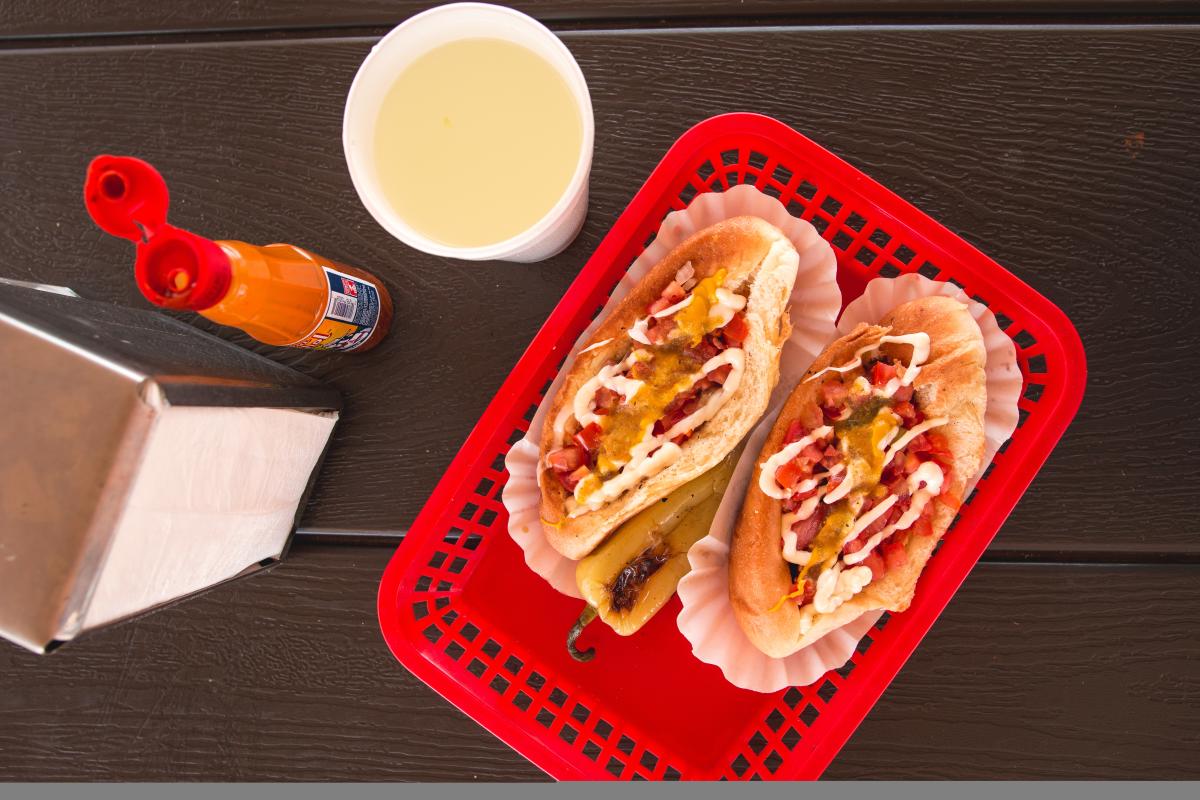 photo of two sonoran dogs, a drink and hot sauce