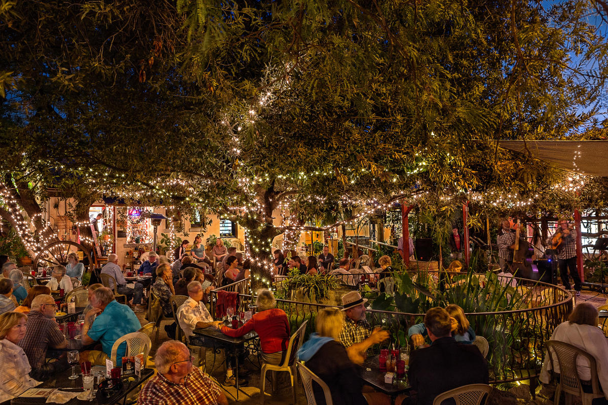 Large outdoor dining arrangement filled with people. String lights wrapped around trees light up the night