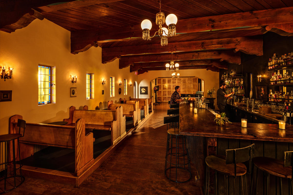 Dimly lit bar with old wood booths, stained glass windows and large bar with stools
