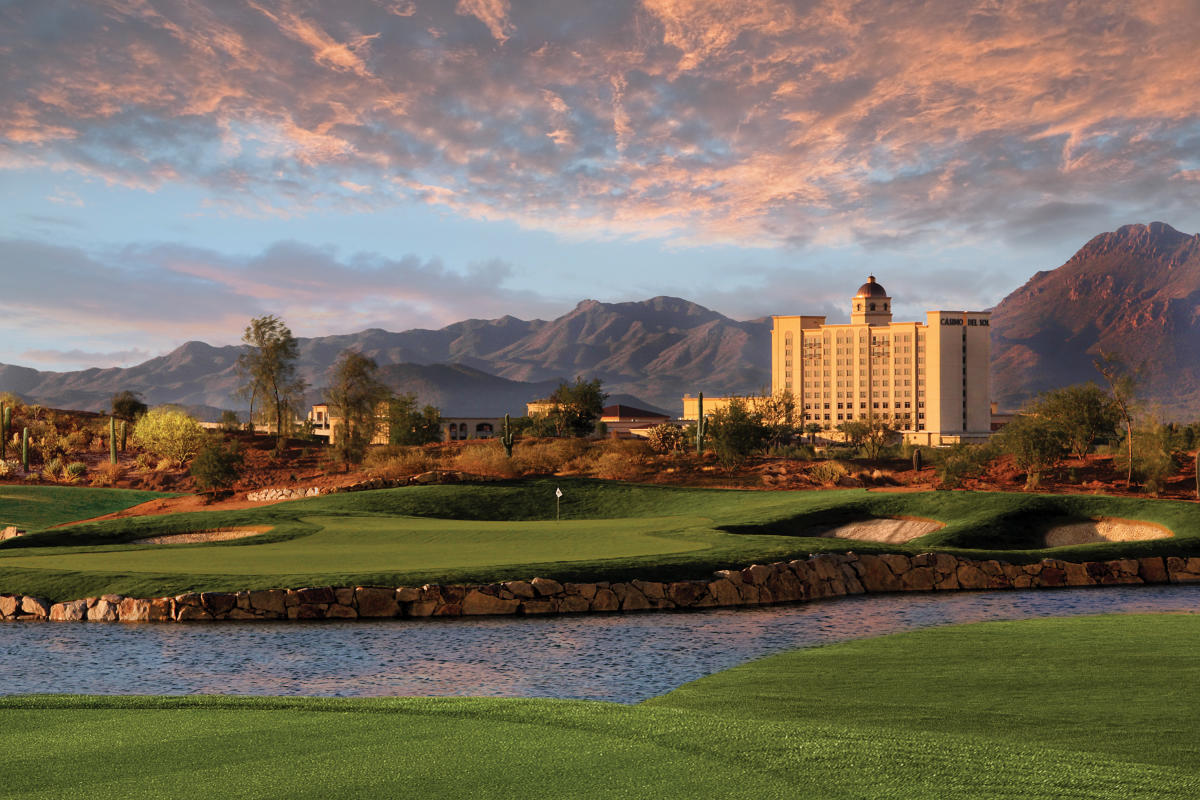Exterior of Casino Del Sol, Wide shot showcasing the green landscape and pond of the Sewailo Golf Course. Casino Del Sol stands tall and golden against the desert mountains