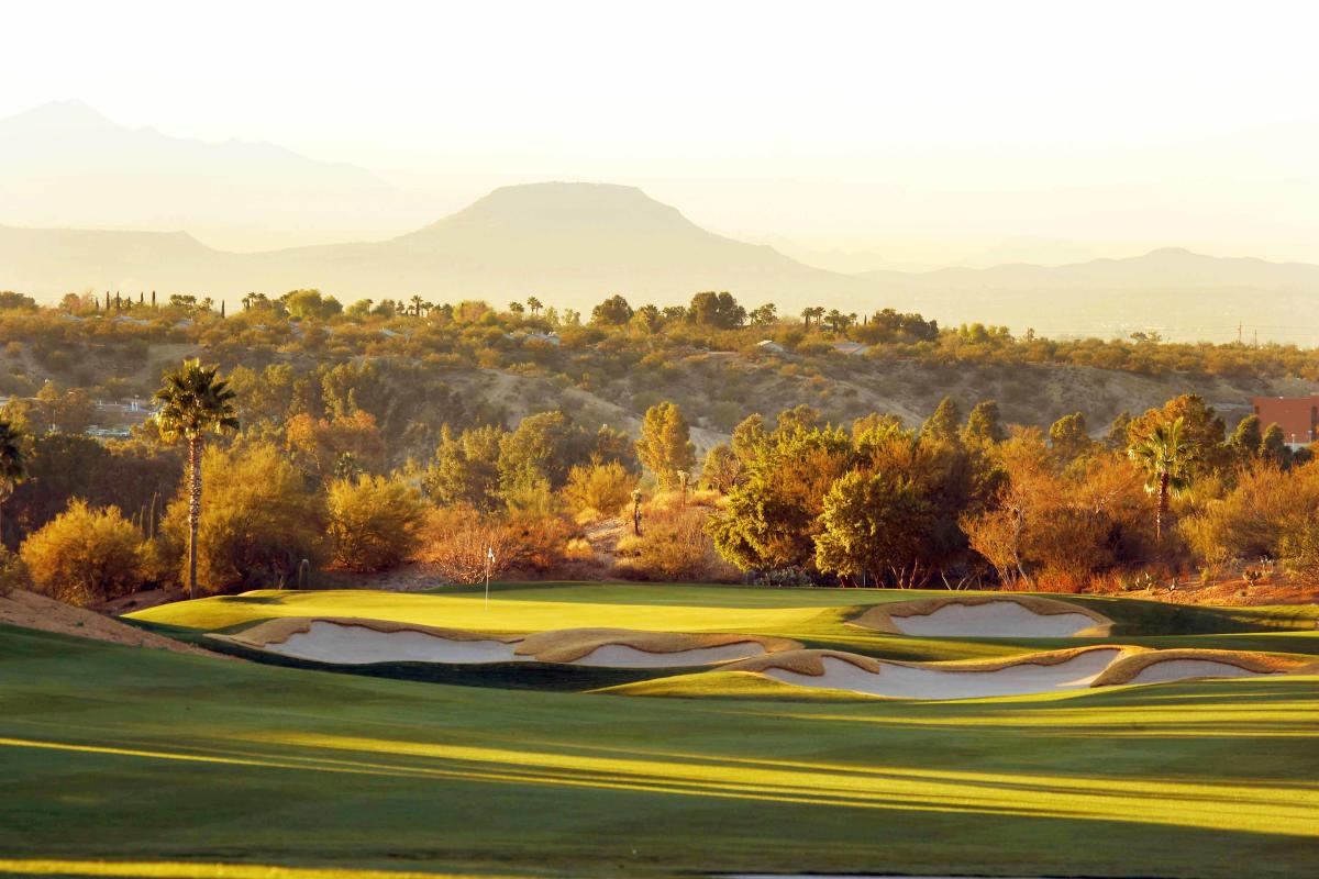 landscaped golf course with bright green grass and sandy valleys with golden desert surroundings
