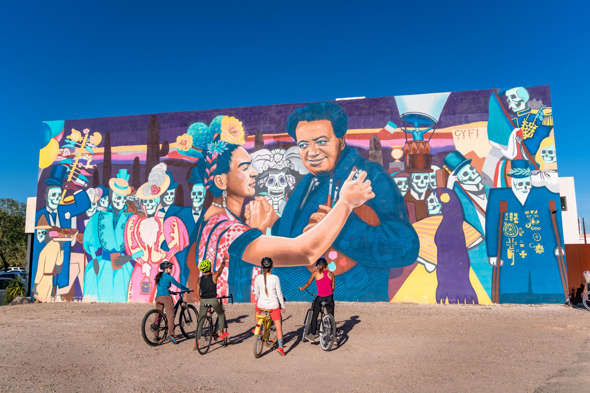 Cyclists look at a mural of Frida Kahlo and Diego Rivera