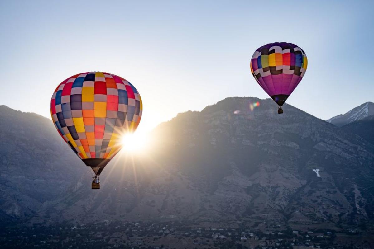 two hot air balloons in the sky with provo mountains and sunrise behind
