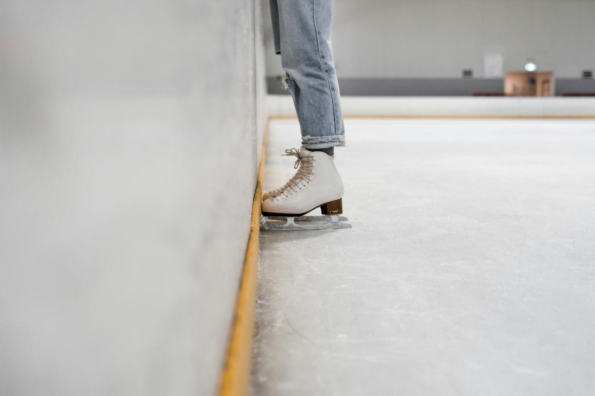 ice skater wearing jeans leans against side of the rink