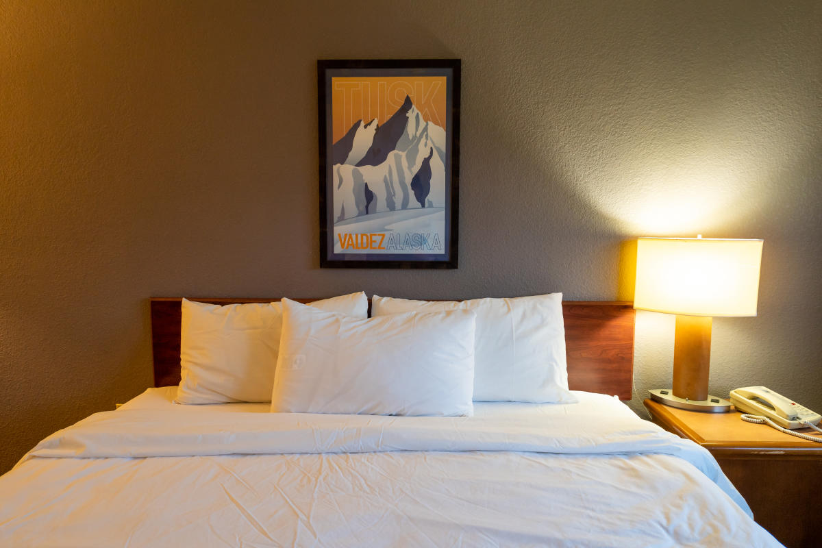 a hotel bed with a poster above the bed of mountains in Valdez, Alaska