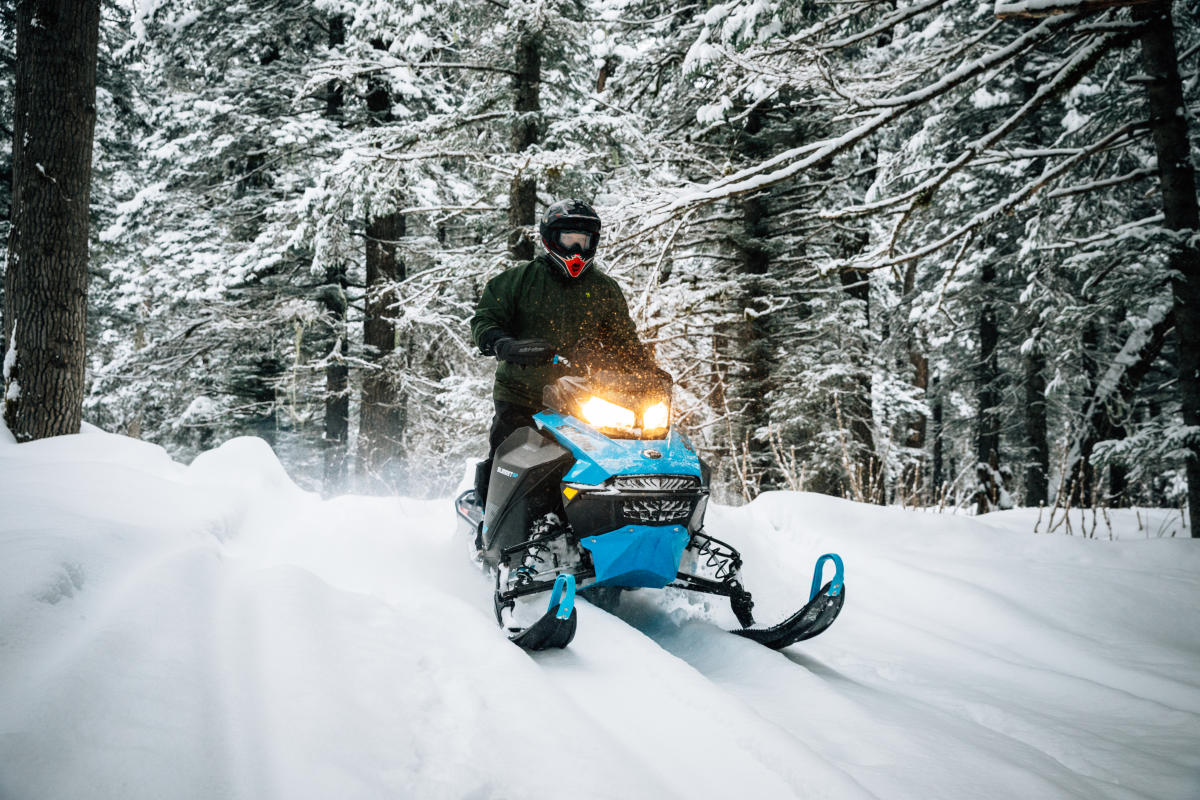 a snowmachiner riding through a winter forest trail