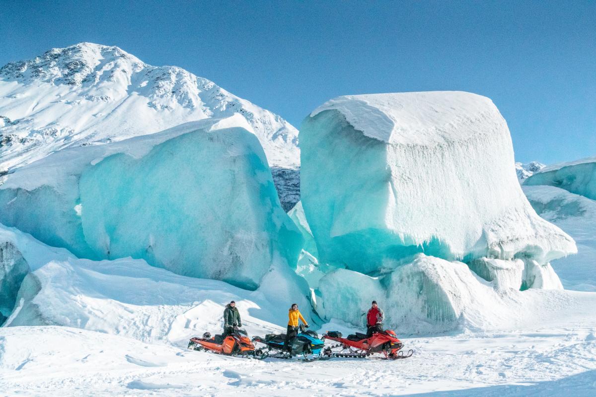 three snowmachiners standing in front of an iceberg