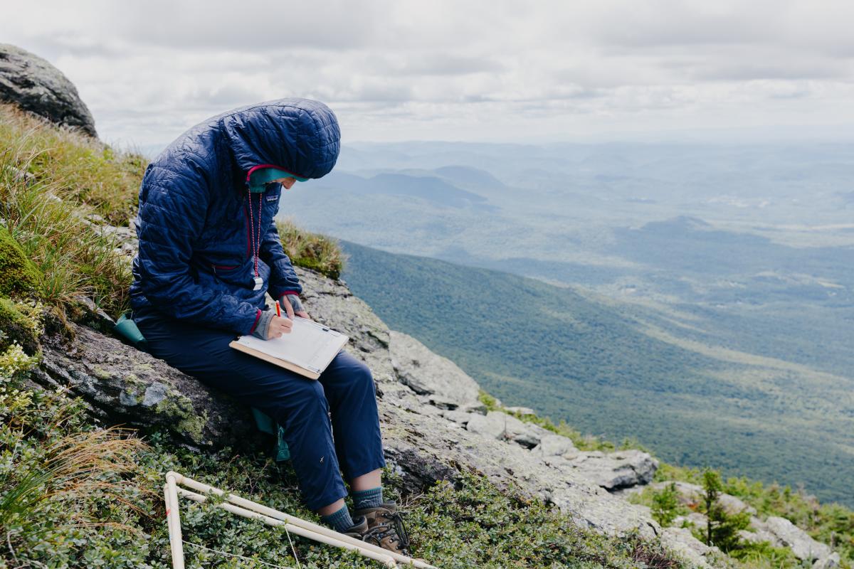 Student on top of mountain studying notebook