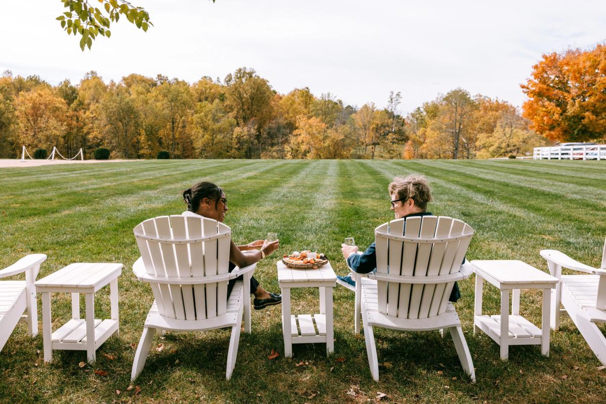 Two people sip cider in Adirondack chairs at Castle Hill Cider