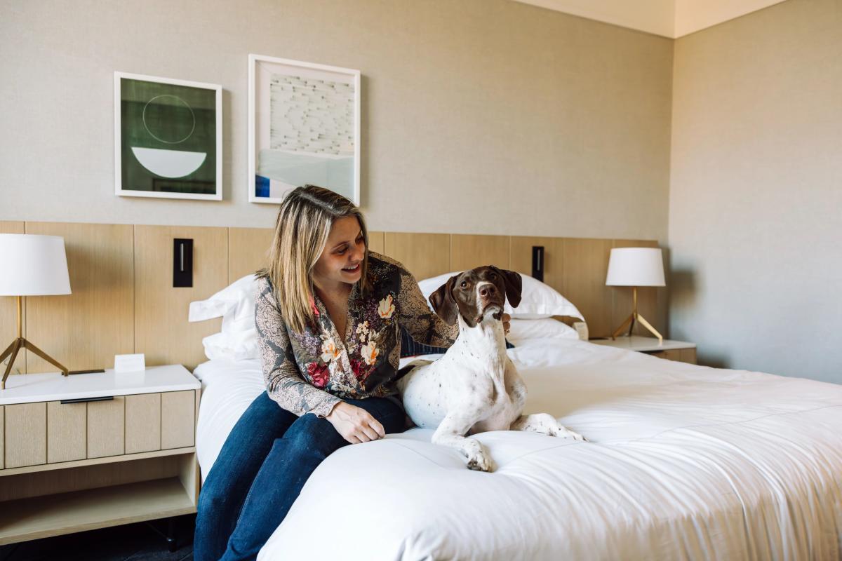 A dog and owner sit on the bed at the pet-friendly Kimpton The Forum Hotel