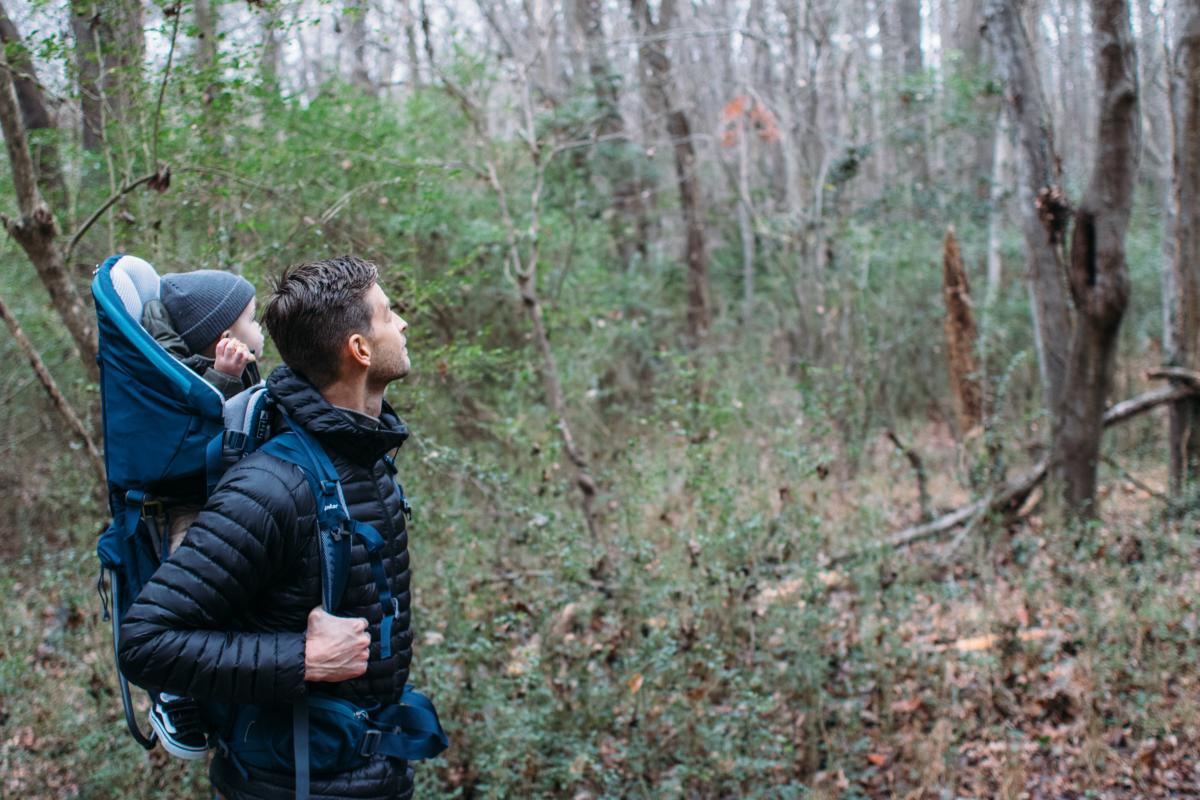 man carry baby in backpack carrier hiking in woods