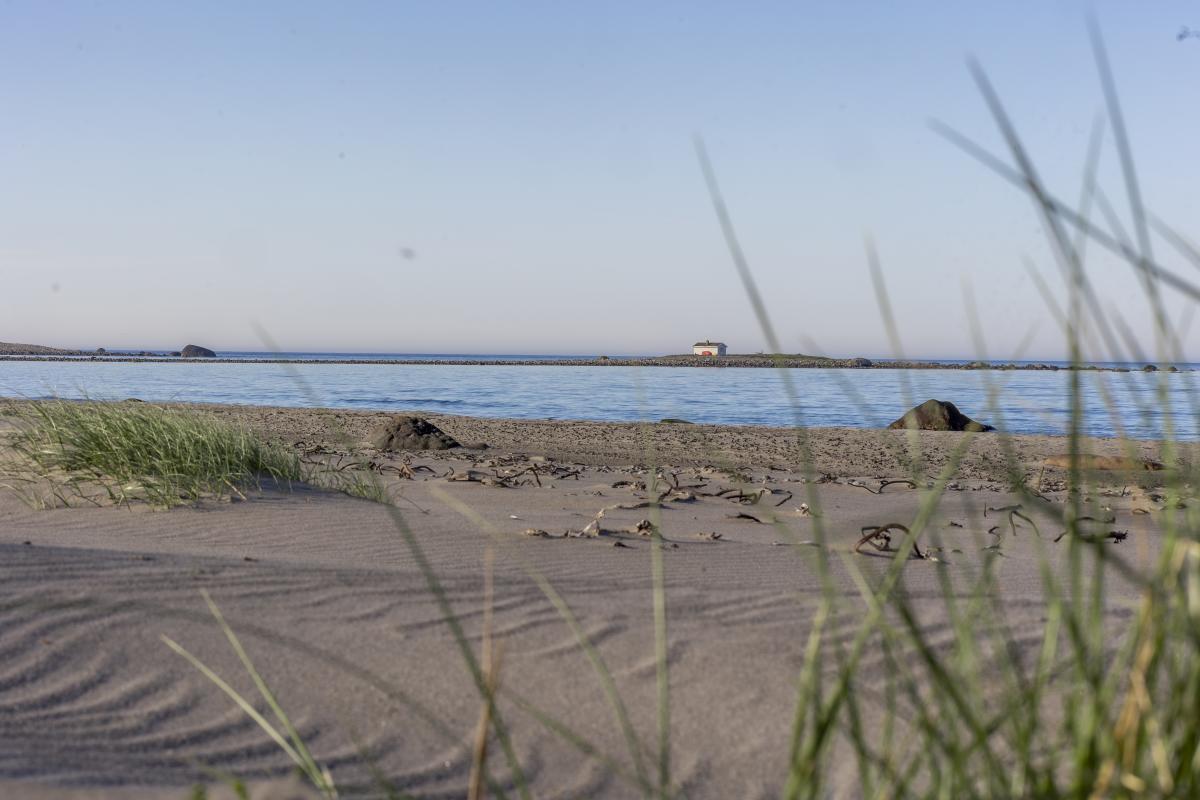 Bilde tatt fra Nordhasselvika og utover mot havet, man kan se bølgene på en stille dag og et lite, hvitt hus med røde karmer