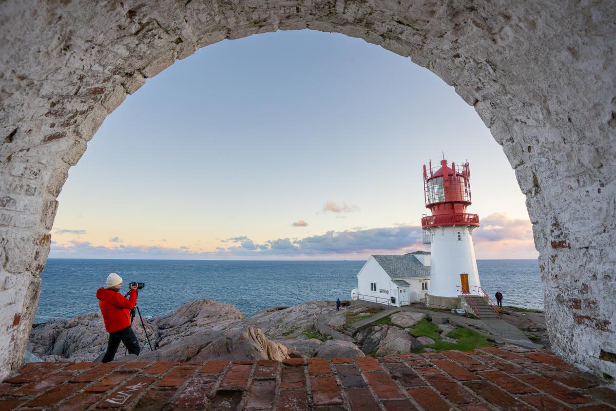 Kvinne i orange jakke fotograferer Lindesnes Fyr