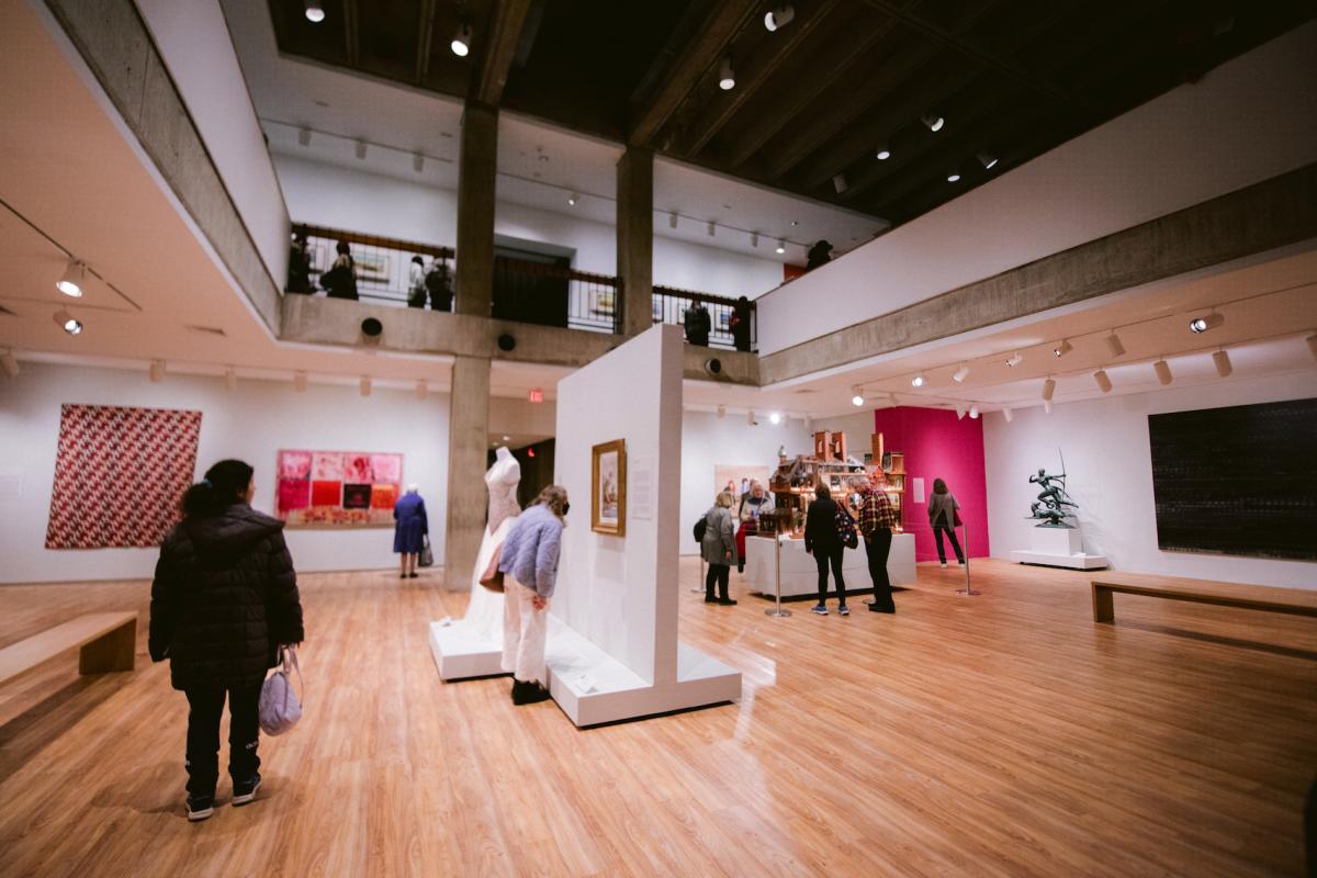 Several patrons visit an art gallery at the Hudson River Museum. The art is hanging on the walls around the room.