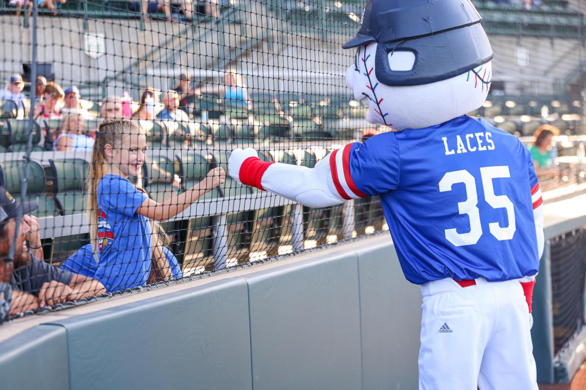 A girl gives the NBC mascot knuckles through the fence at the stadium during the NBC World Series.
