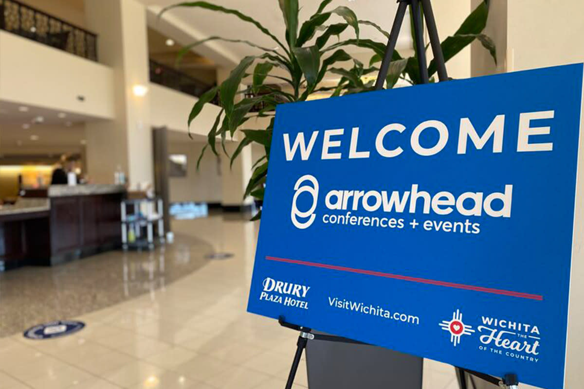 A blue sign with white text reads "Welcome Arrowhead Conferences & Events" in the lobby of the Drury Hotel