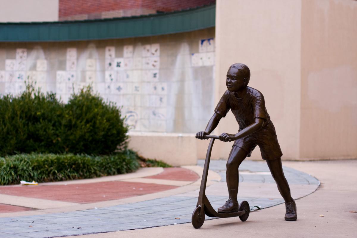 A bronze sculpture of a boy on a scooter sits in downtown Wichita