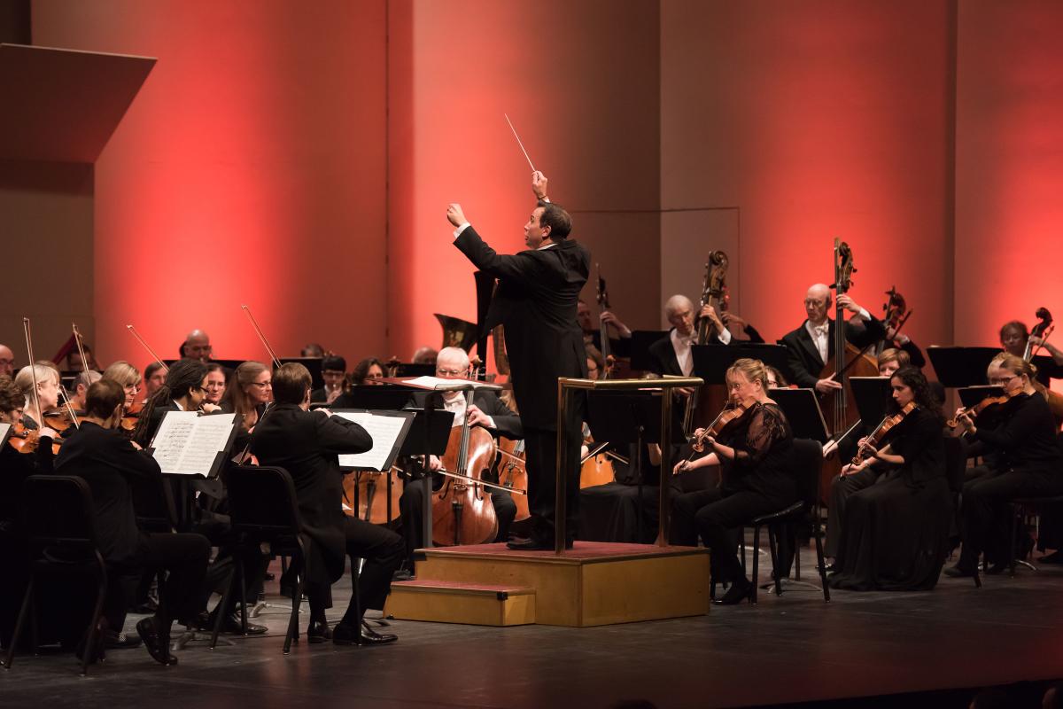 A conductor raises his arms while symphony member of the Wichita Symphony Orchestra play