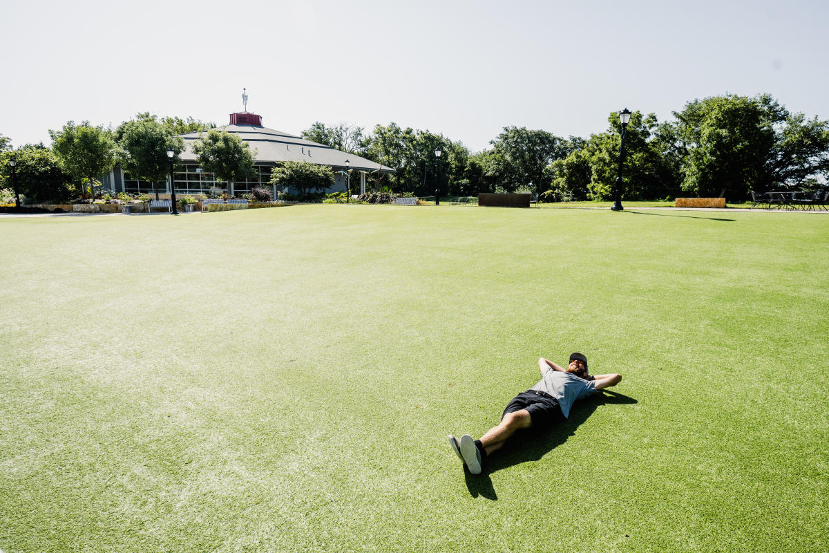 A man lies on the turf at near the theater at Botanica Wichita on a sunny day.