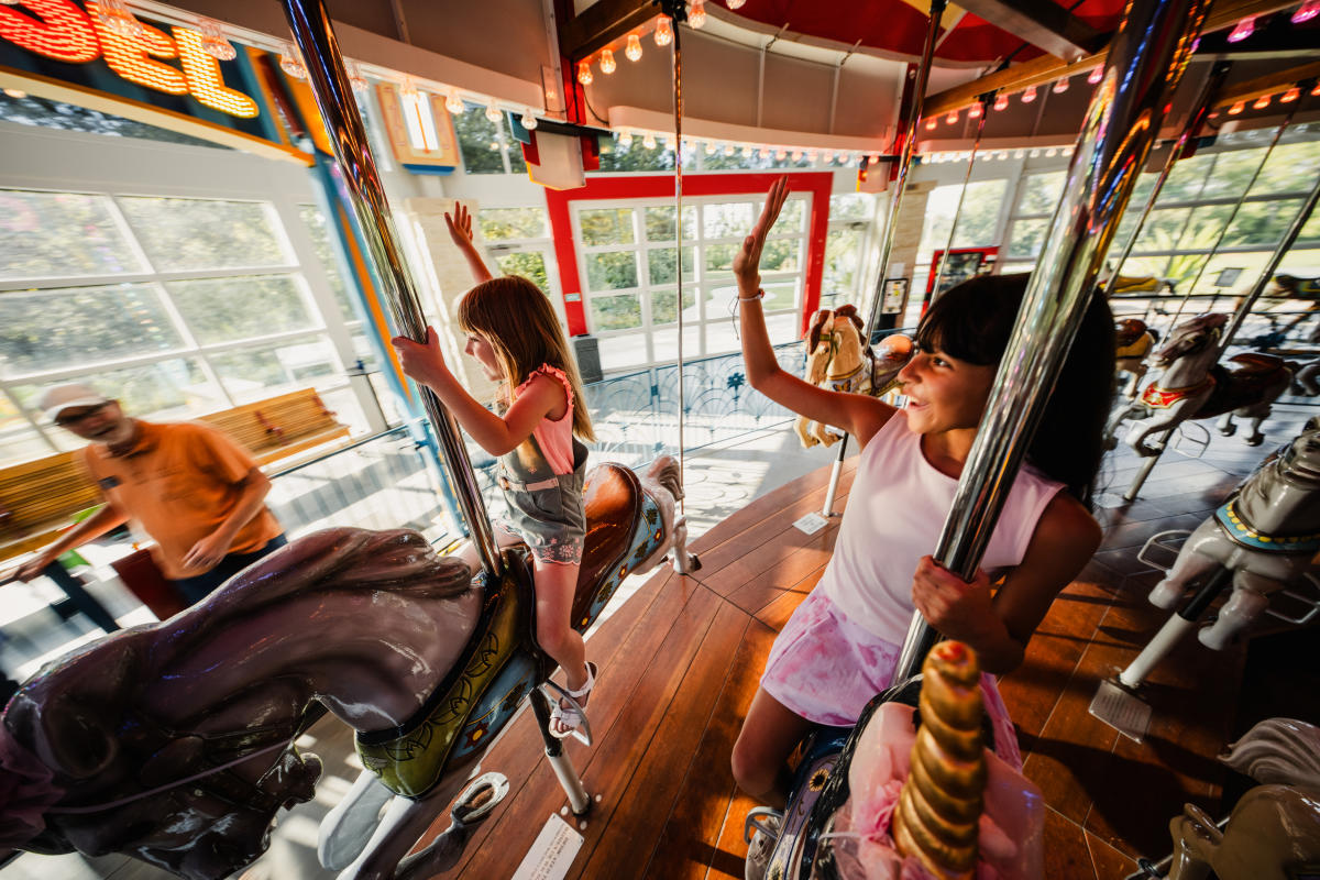 Two girls wave and smile while riding the carousel at Botanica Wichita.