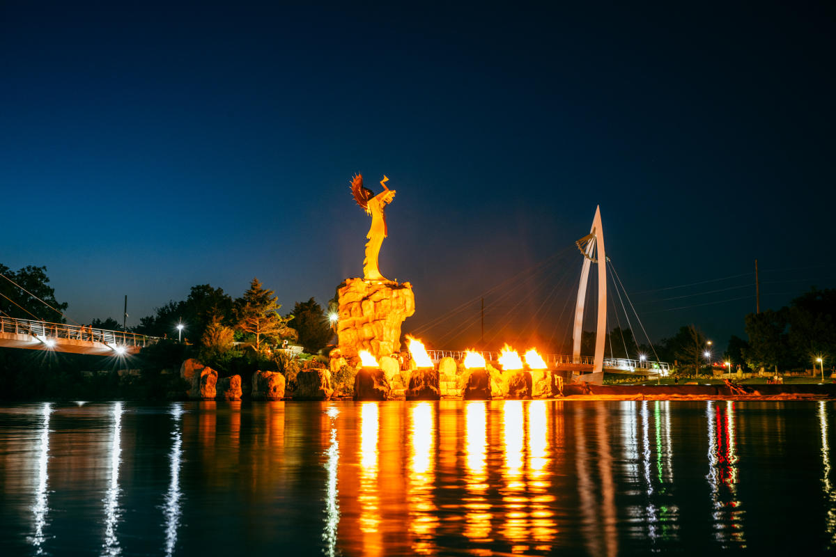 The Keeper of the Plains rests along the river with the firepots lit at its base.