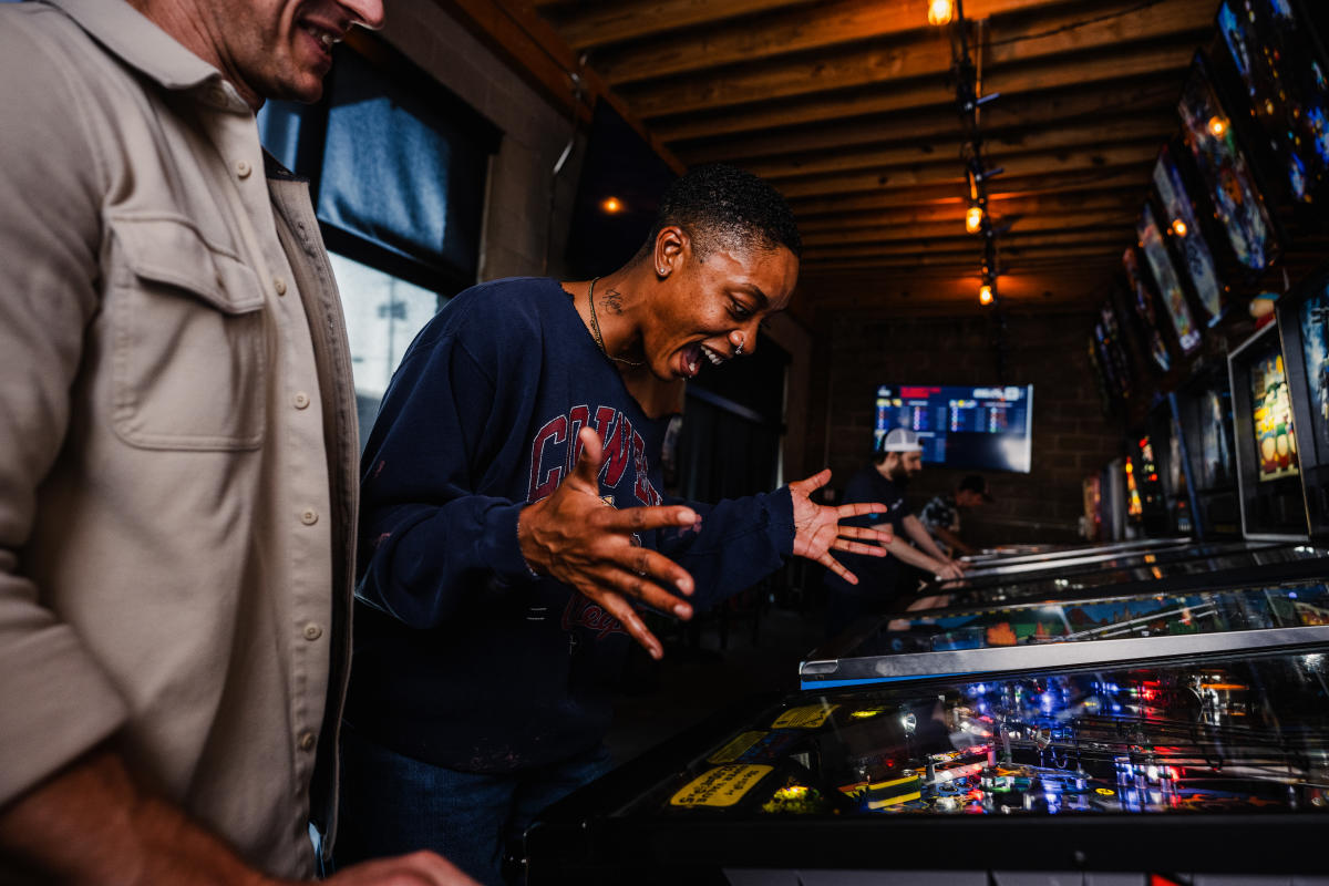 A woman shouts and smiles as she plays a vintage pinball game at The Arcade in Wichita.