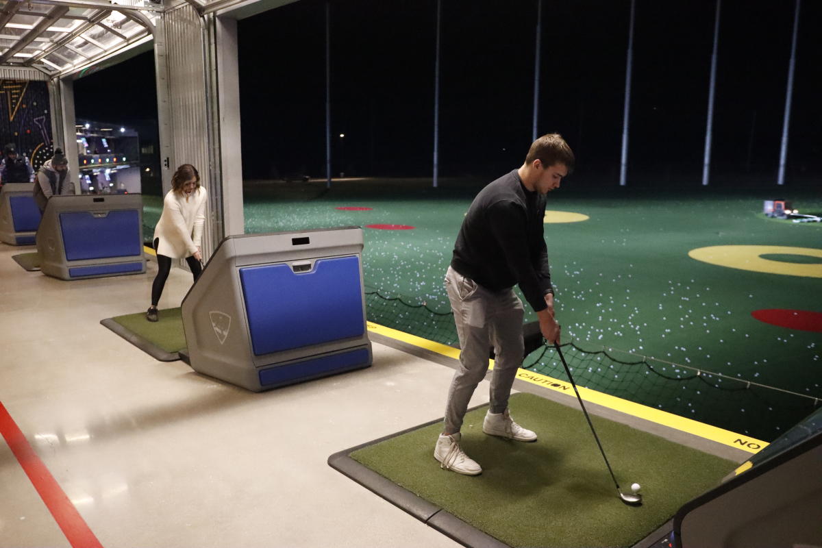 A man and woman each swing at side-by-side bays at Topgolf