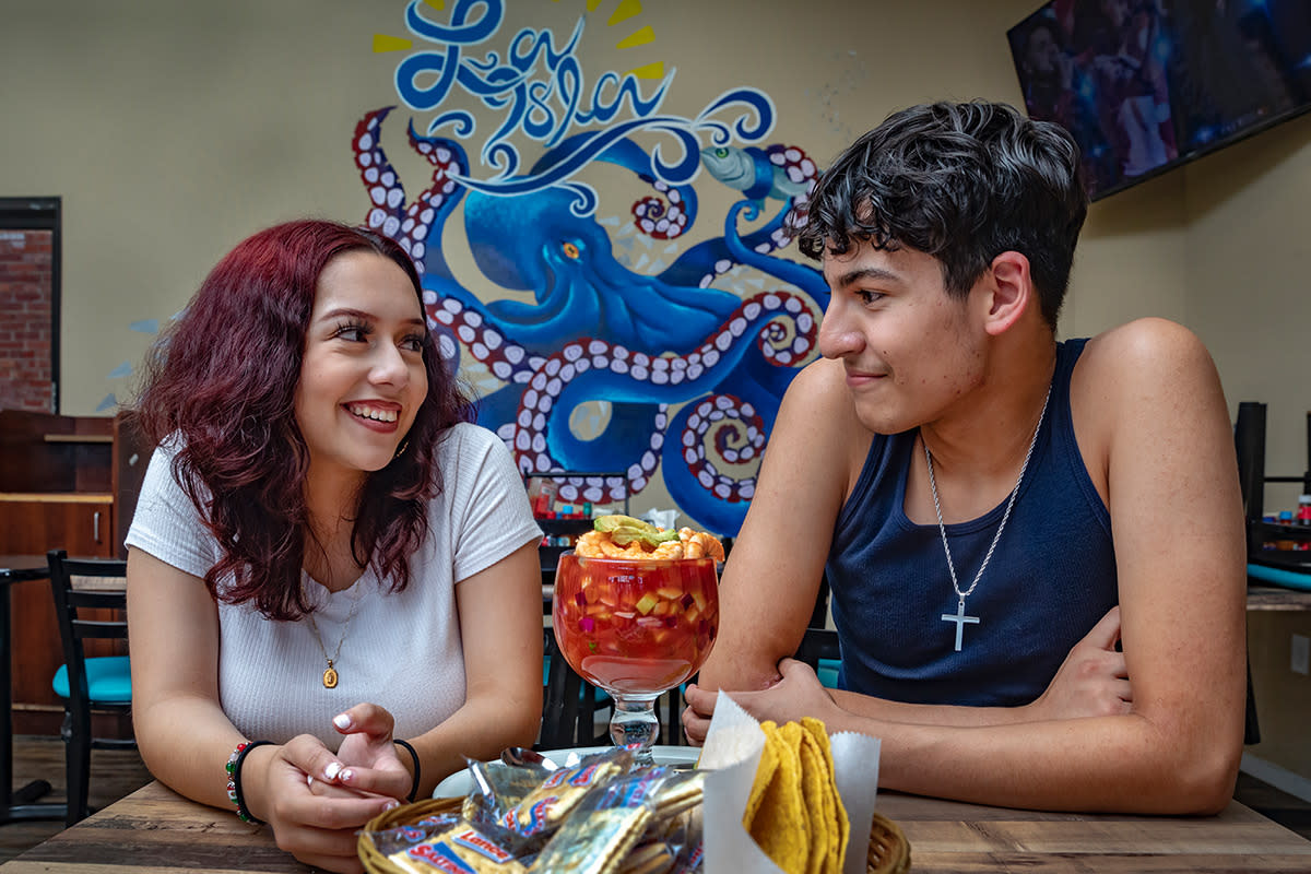 A young Hispanic woman and man smile at each other over shrimp ceviche