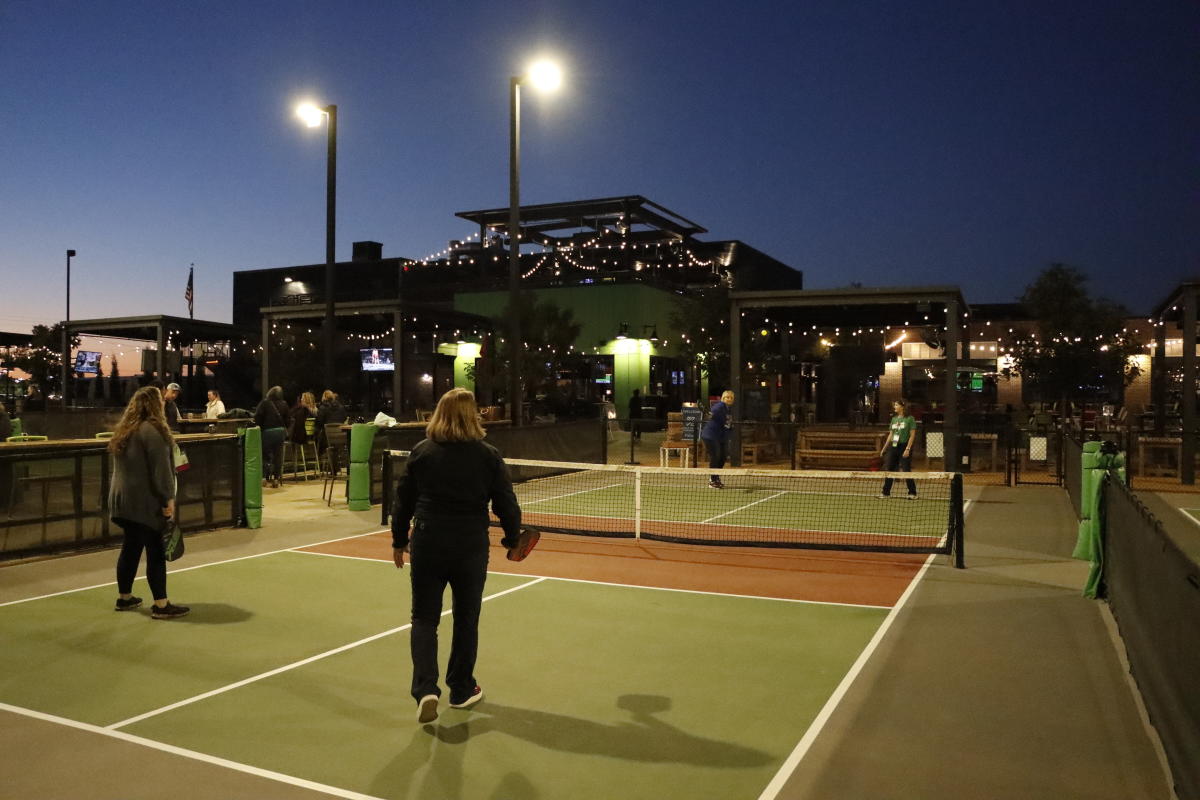 A group of meeting attendees play outdoor pickleball at night at Chicken N Pickle