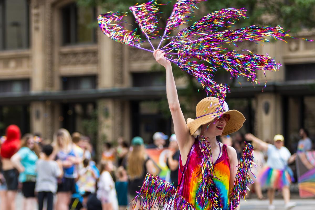 A woman waves metallic fans while walking in the Wichita Pride Parade