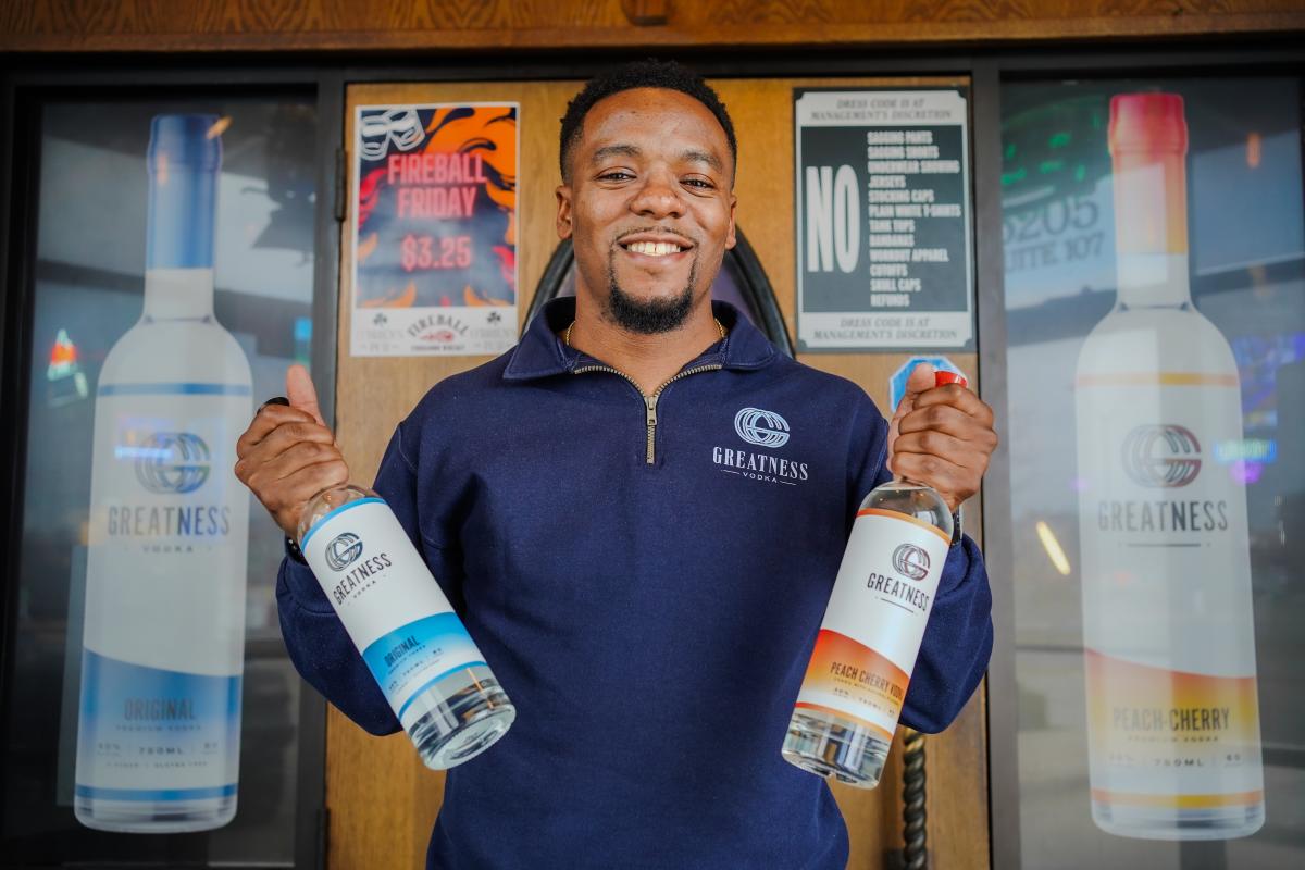 Troy Brooks poses holding a bottle of his Greatness Vodka in each hand