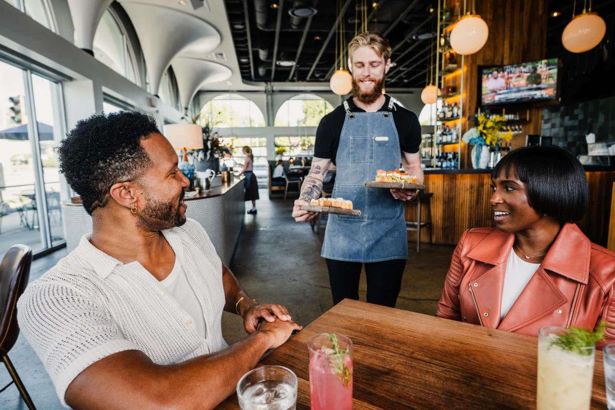 A man and woman smile while a server presents food to their table at The Belmont.