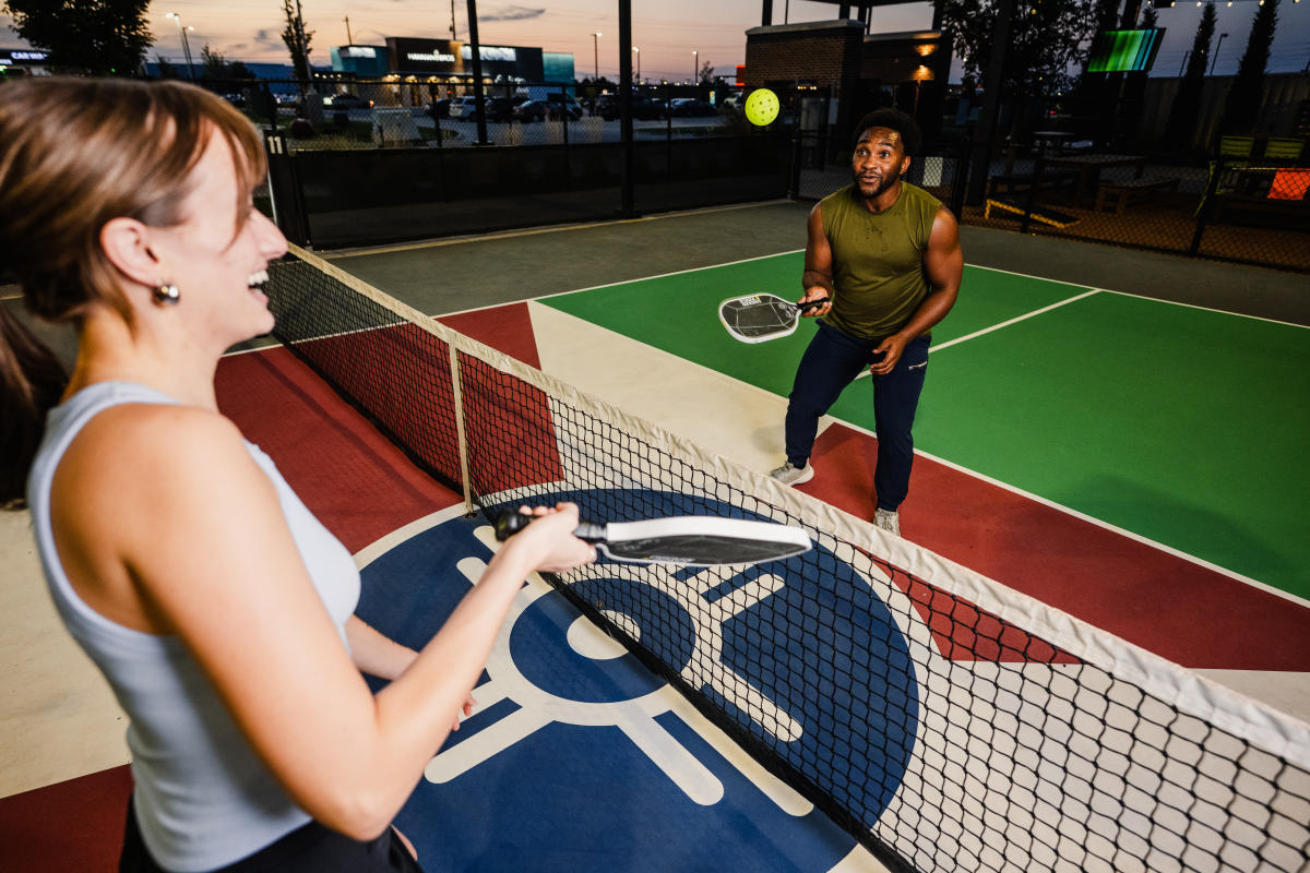 A man and woman smile while enjoying a game of Pickleball at Chicken N Pickle.