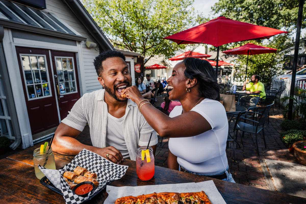A man and woman smile while she feeds him a slice of pizza on the patio at Ziggy's Pizza.