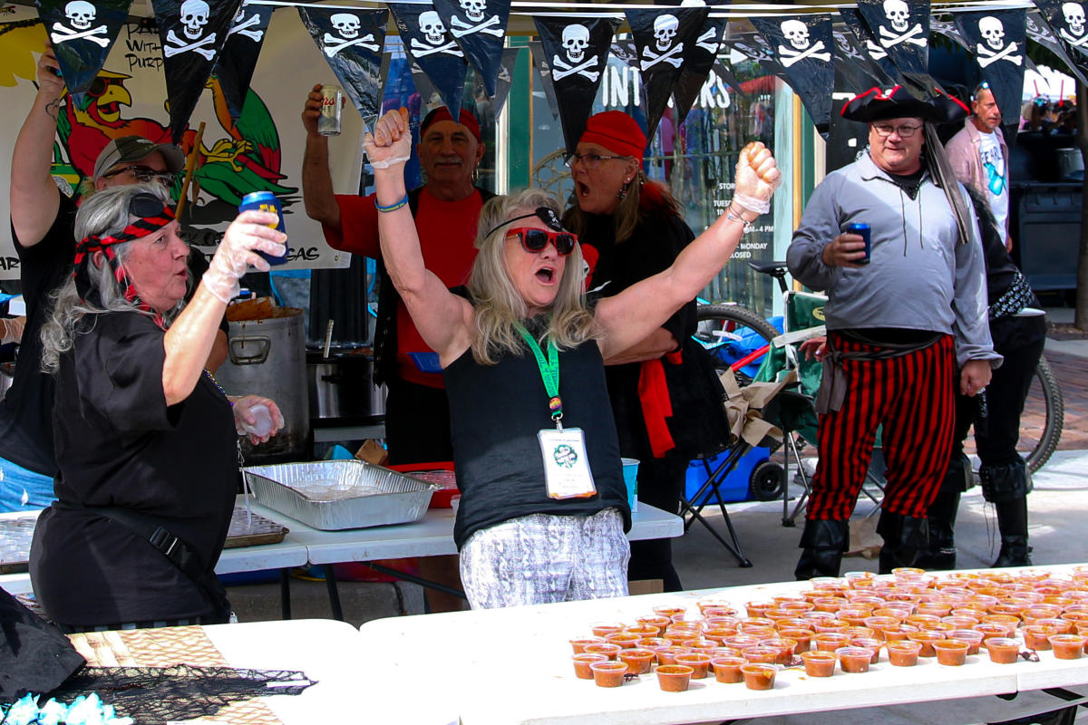 A woman raises her fists and cheers at her chili booth at the Wagonmasters Downtown Chili Cookoff