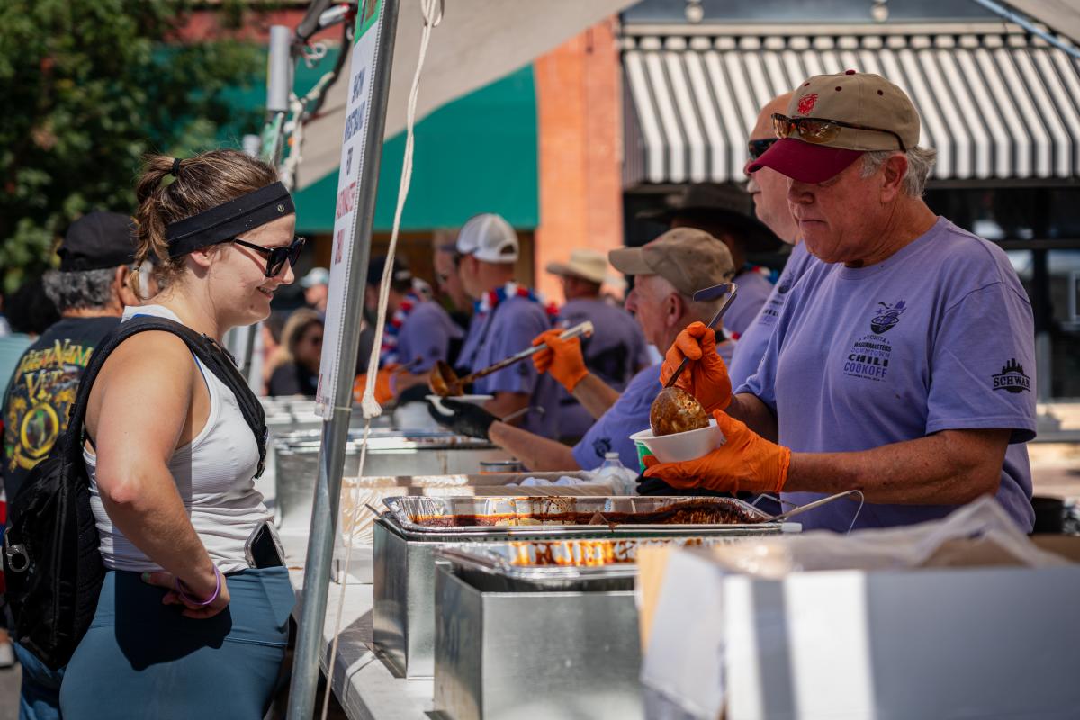 A man serves a woman chili during the Wagonmasters Downtown Chili Cookoff