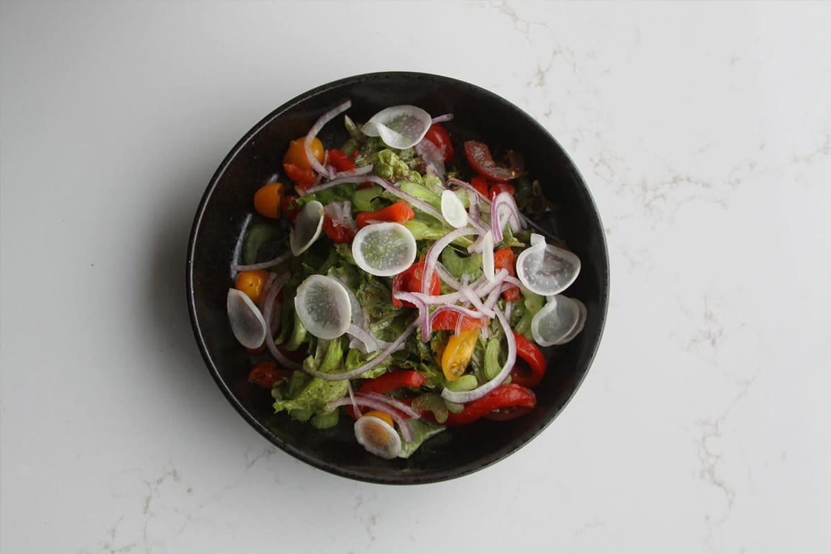 A fresh salad topped with onions and peppers is served at First Mile Kitchen