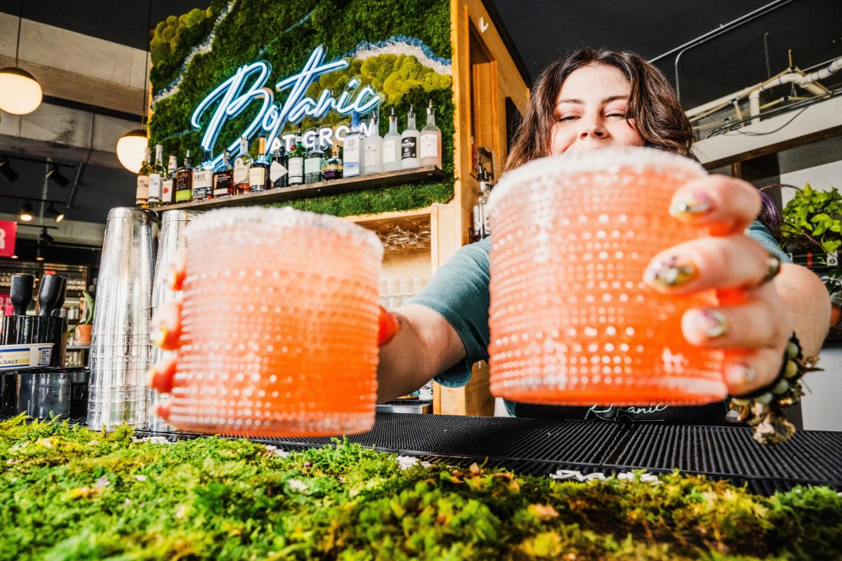 A woman serves two drinks at the bar inside GROW Plant Bar