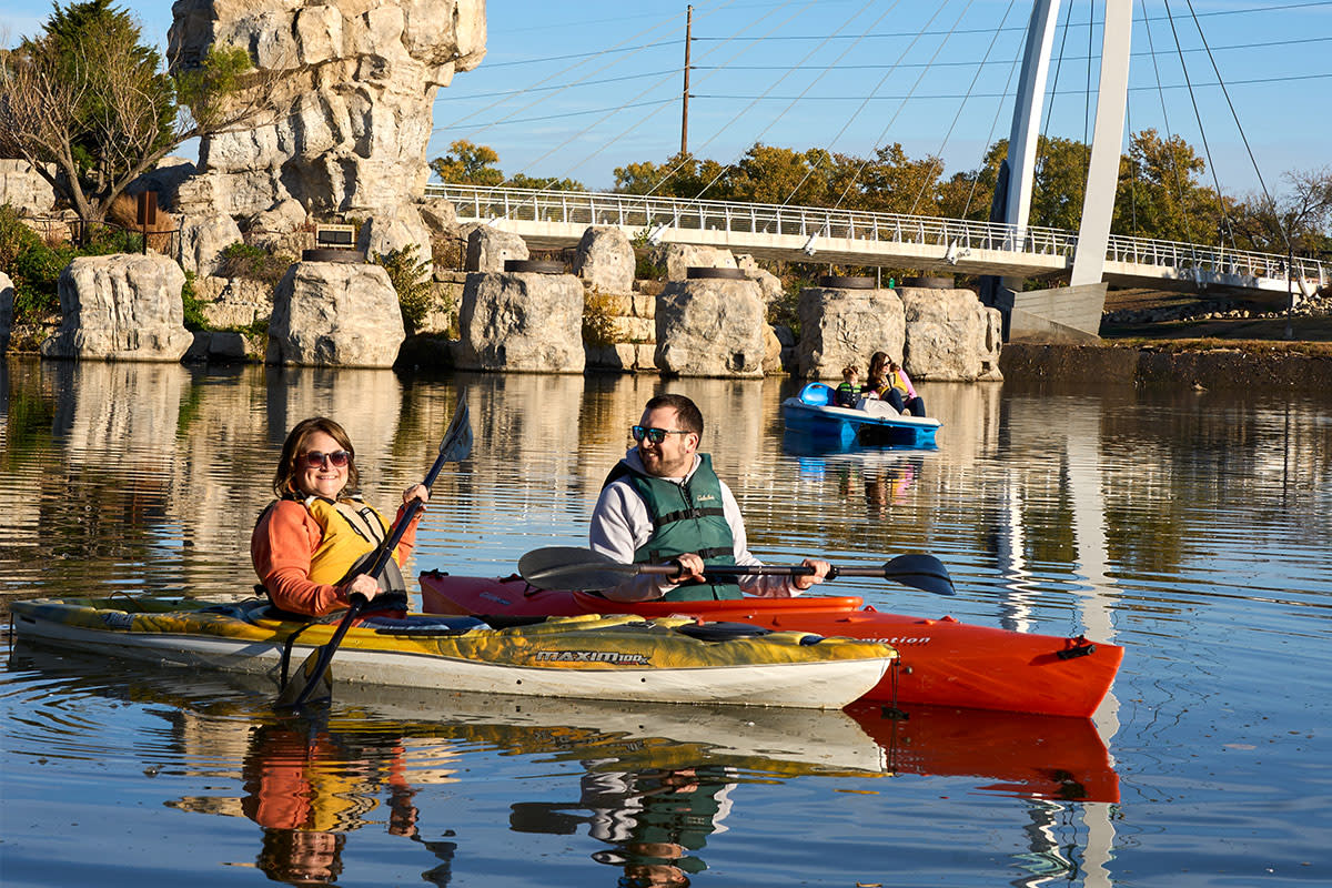 A man and woman kayak on the Arkansas River near the Keeper of the Plains