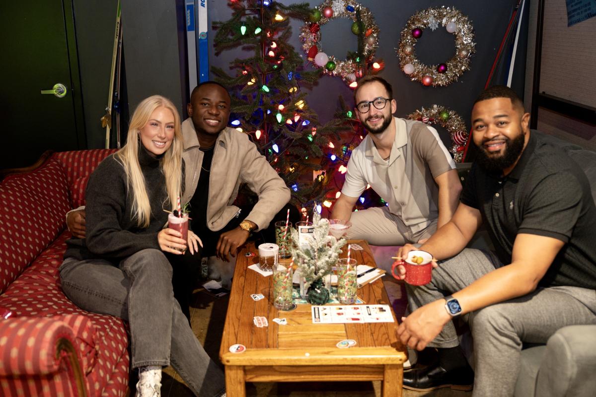 Four adults pose for a photo inside the holiday hideaway pop-up bar at Chicken N Pickle